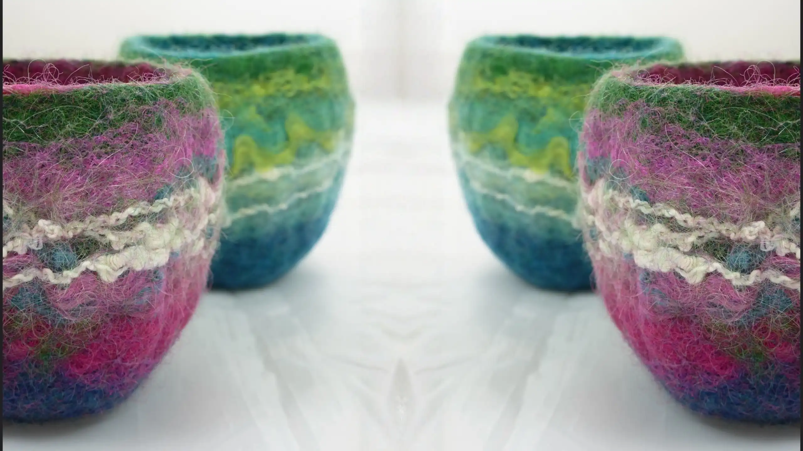 Close-up of handmade felted bowls arranged on a light surface. The bowls feature vibrant blended colors including pink, purple, green, turquoise, and blue, with textured wool fibers.
